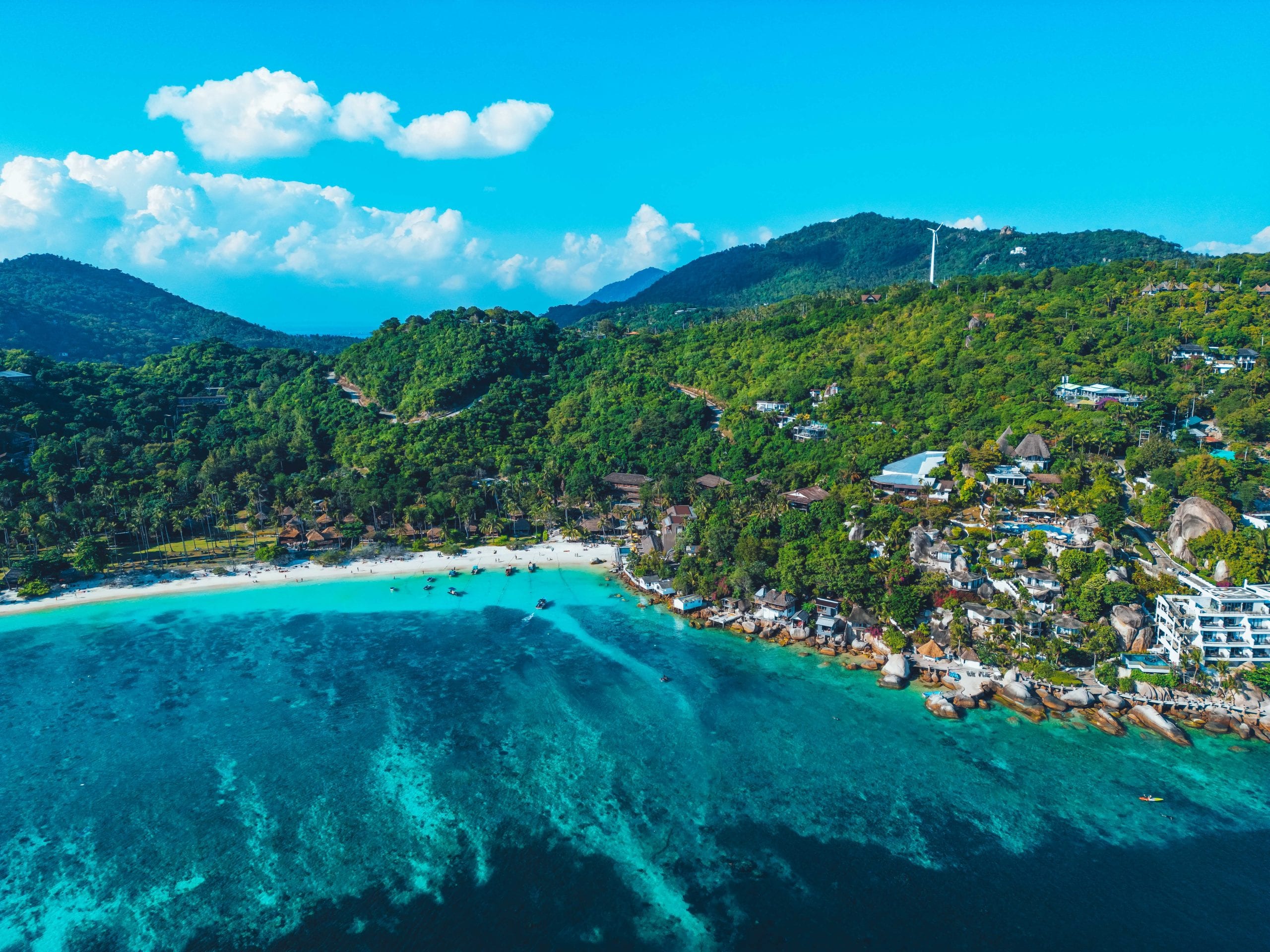 The west coast of Koh Tao seen from above, resorts set back behind a shallow reef