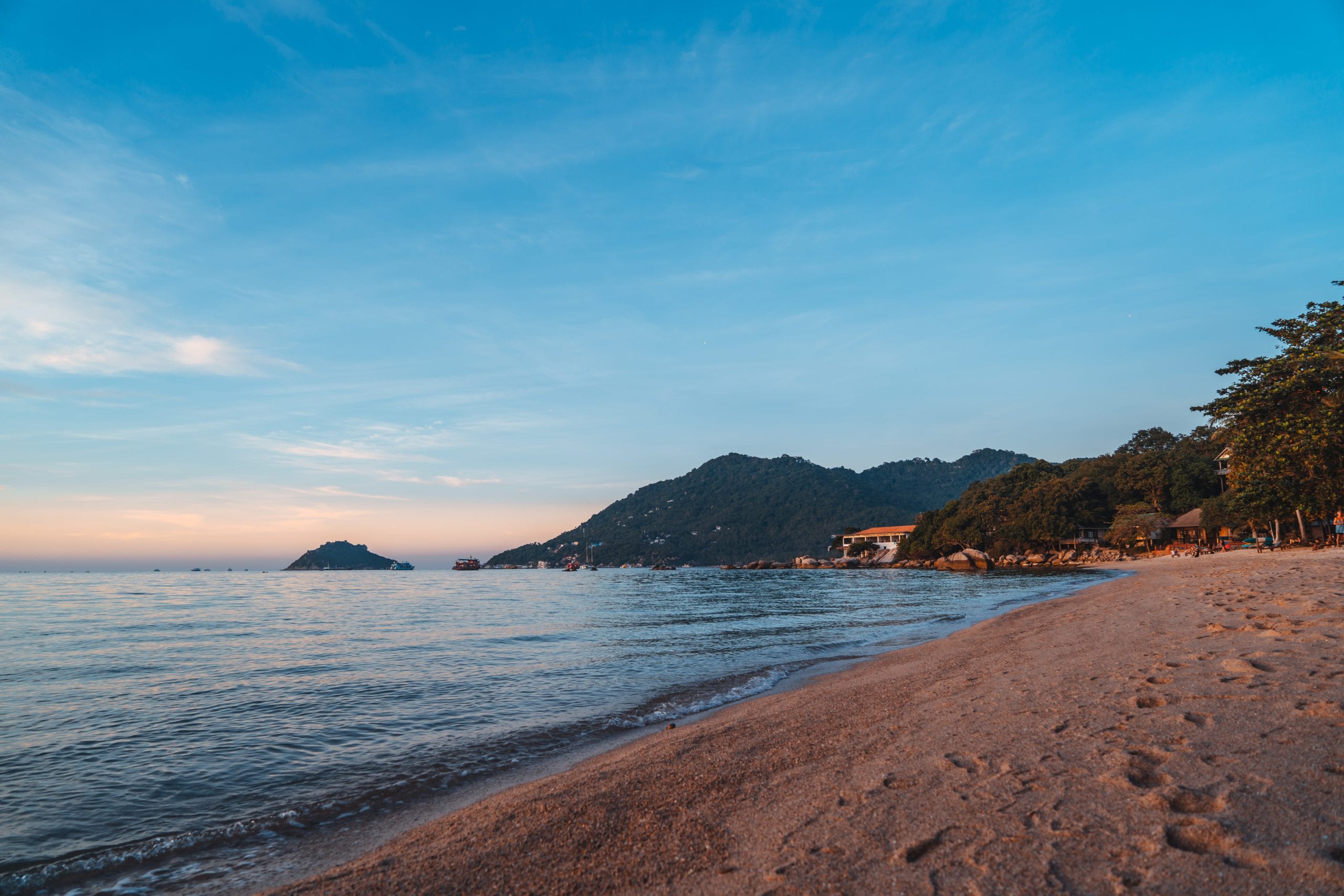 A curved Koh Tao bay with an island offshore, calm and shallow near the sand