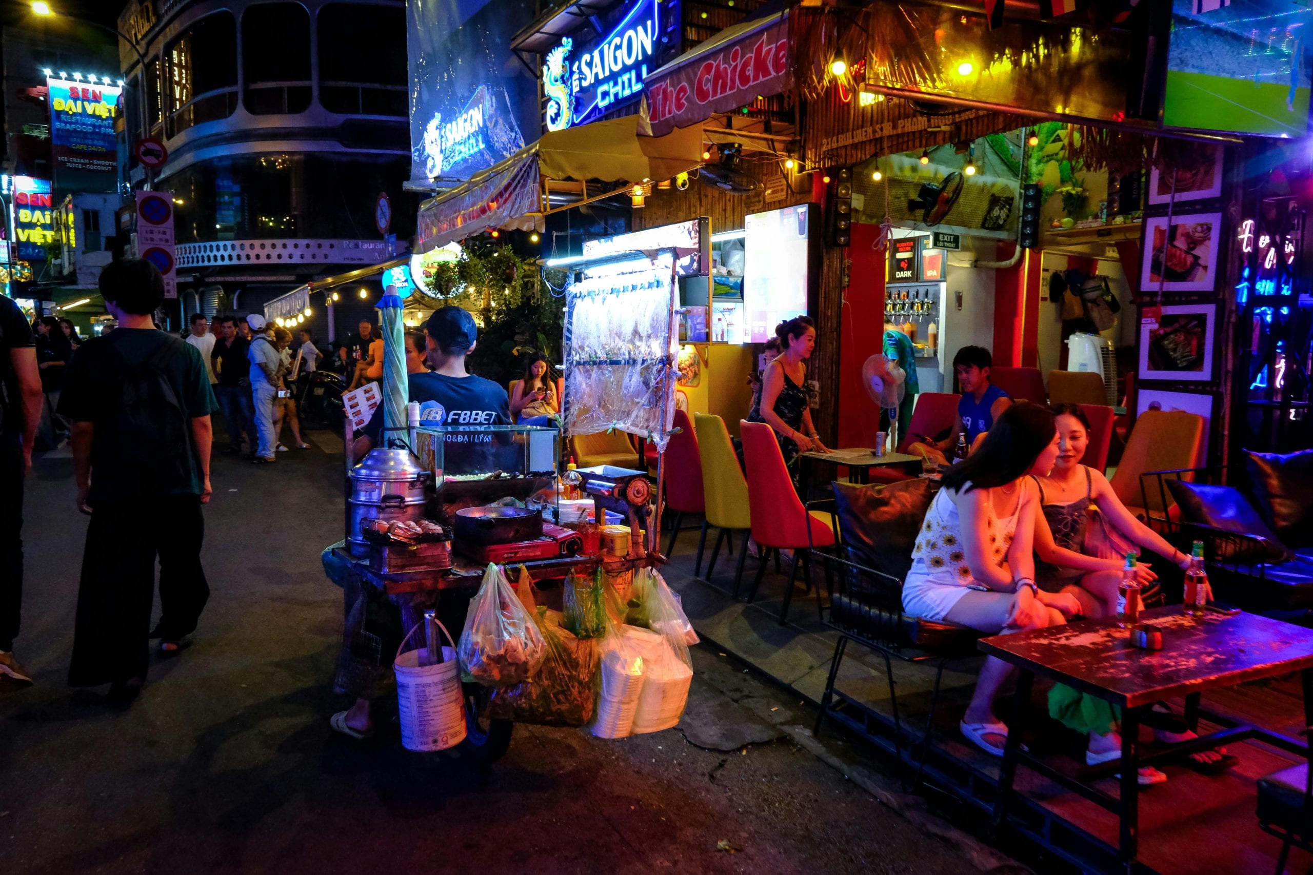 A Thai food street after dark, grills and plastic stools